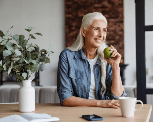 Mujer sonriente con cabello blanco sosteniendo una manzana.