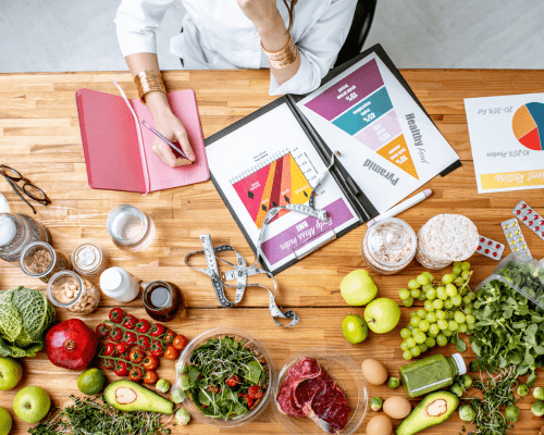 Persona realizando un plan nutricional sobre una mesa llena de alimentos saludables.