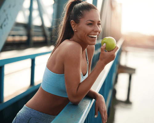 Mujer saludable en ropa deportiva comiendo una manzana en un puente.